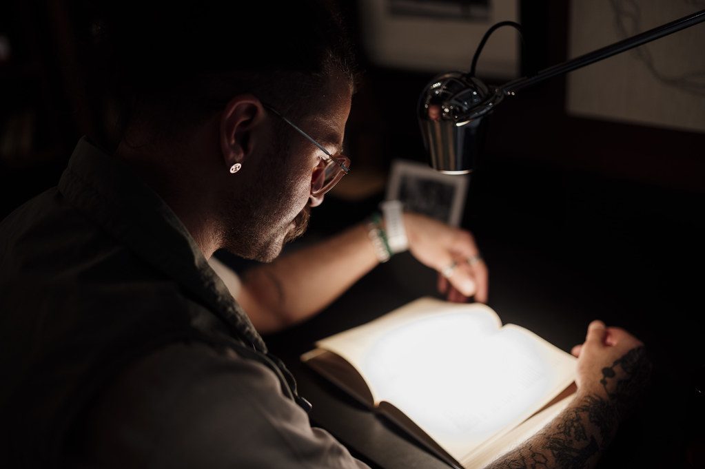 Young man reads a book under a lamp in a dimly lit room