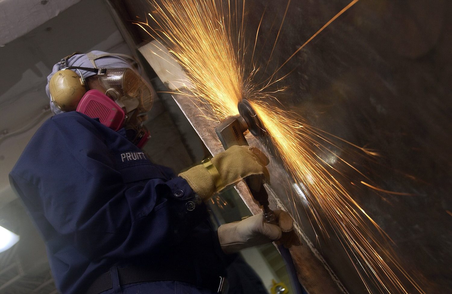 US Navy 041005-N-1485H-085 Seaman Angel Pruitt of Dayton, Ohio, uses a pneumatic wire wheel grinder to remove old paint and rust from a bulkhead in the forecastle of the conventionally powered aircraft carrier USS Kitty Hawk (C